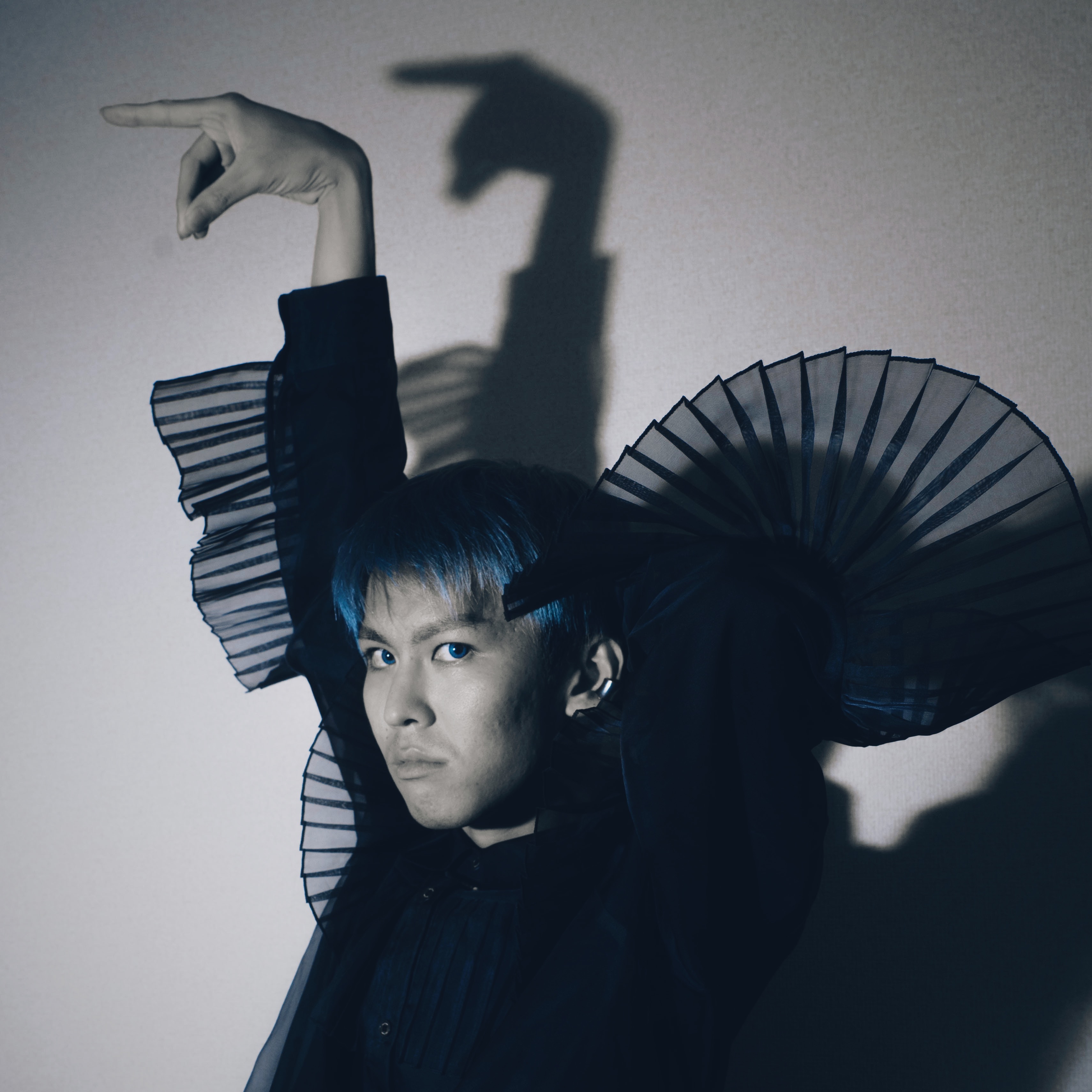 Shunya Takabayashi。片手を上げ、壁に落ちる手の影とともに写るポートレート。